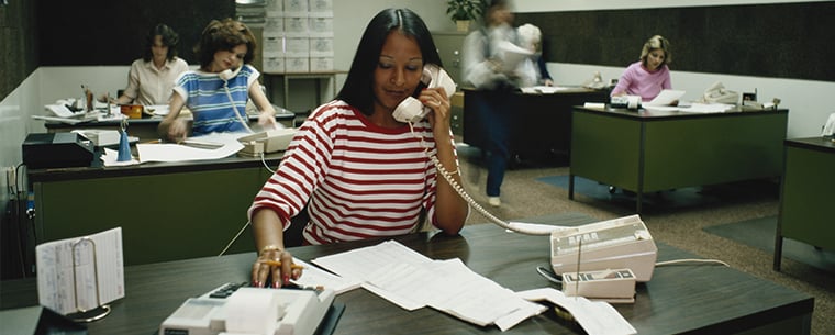 1980s era office with women working at desks on typewriters and phones