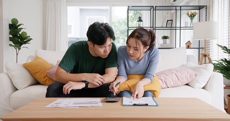 young couple sitting in their living room looking at bills with a calculator